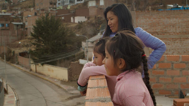 An Andean woman and two children look at the view over a short brick wall on an elevated building.