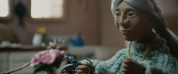 A claymation figure of Elder Colleen Hemphill, seated and holding a fish hook.
