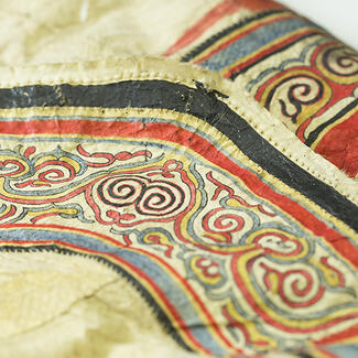 Detail of leather piece of clothing, showcasing the ornate and colorful stitching along the border.